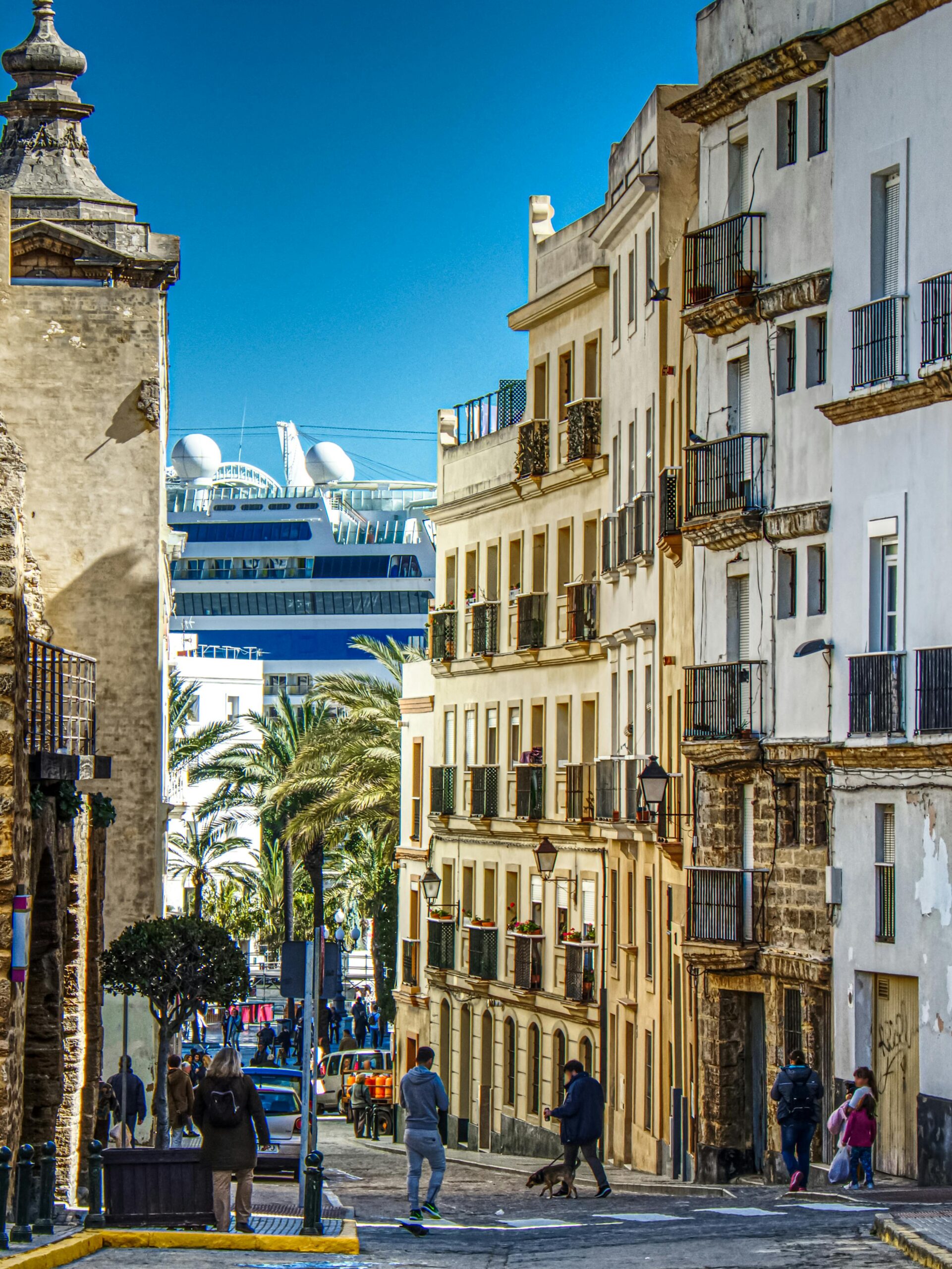 Street view of Cádiz, Spain, showcasing vibrant urban life with a cruise ship in the background.